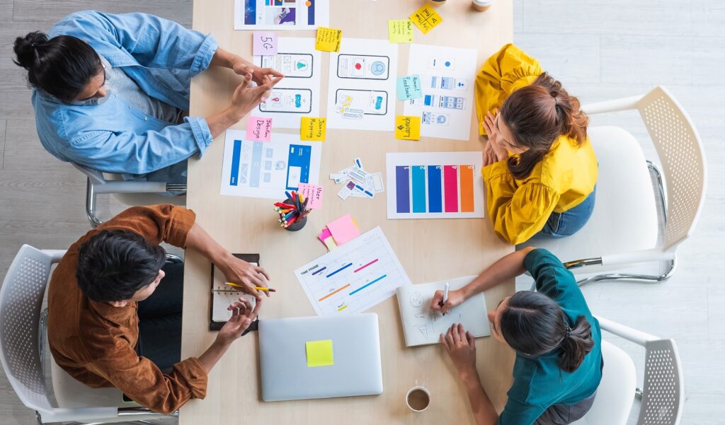 Top view ux developer and ui designer brainstorming about mobile app interface wireframe design on table with customer breif and color code at modern office.Creative digital development agency